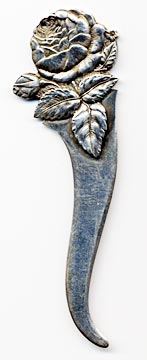 This bookmark was manufactured in the US by Towle Silversmiths. It is marked with the familiar hallmark of the T enclosing a lion along with Sterling and the number 6. On top of the 6 is stamped the number 17. This is a very interesting piece because the front is a very detailed relief of a rose and the back has a scored picture of a woman with a feather hat. The date is 1890 - 1920.