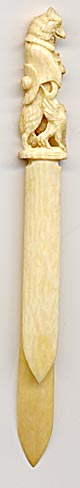 This bookmark is made in a European country probably between 1900 - 1920. It is made of ivory with a hand carving of a wolf dressed as padre holding a cross in one paw and a chicken in the other. It is possibly from a fairy tale.
