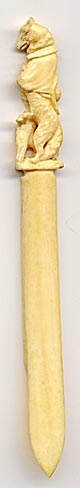 This bookmark is made in a European country probably between 1900 - 1920. It is made of ivory with a hand carving of a wolf dressed as padre holding a cross in one paw and a chicken in the other. It is possibly from a fairy tale.