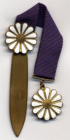 This bookmark was made in Europe. It is made of brass and enamel and has a blue ribbon between the two pieces. The shape is a daisy flower. 