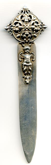 This bookmark was made in the US by Shiebler. It is marked with the makers hallmark of a winged letter S and sterling. The top is an ornate 3D design and an angel/cherub forms the top blade of the bookmark.