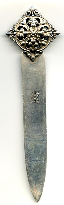 This bookmark was made in the US by Shiebler. It is marked with the makers hallmark of a winged letter S and sterling. The top is an ornate 3D design and an angel/cherub forms the top blade of the bookmark.