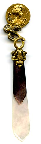 This bookmark was probably produced in France. It is made of mother-of-pearl and gold plate over pot metal. It has two sided coin of women heads held up by an iris flower. The blades are light and dark MOP. The date is 1880 - 1900.