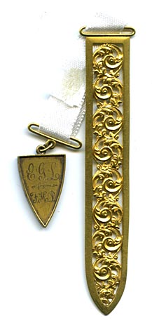 This two piece bookmark has an engraved charm marked on the front  E.G. L. from F.H.P., and on the back XMAS '94. A white satin ribbon is attached to both parts. The blade is a gold color metal with ornate scroll work and a diamond etched finish.