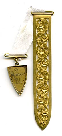 This two piece bookmark has an engraved charm marked on the front  E.G. L. from F.H.P., and on the back XMAS '94. A white satin ribbon is attached to both parts. The blade is a gold color metal with ornate scroll work and a diamond etched finish.