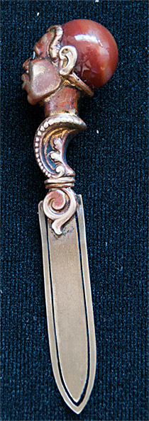 This brass bookmark was made in France by an unknown manufacturer. It depicts the head of an African warrior with diamond eyes and an agate marble head. It has the remnants of a bronze finish.