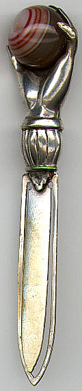 This bookmark was made in Scotland by an unknown manufacturer. It is unmarked and is made of silver plate over brass. It is in the shape of a hand holding an agate marble. The date is probably 1910 - 1920.