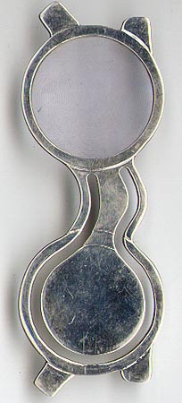 This bookmark was made in the US by Tiffany and Co. It is marked &copy; Tiffany & Co. 925. It is a pair of eye glasses with one side a fresnel lens magnifying glass. The date is 1980 - 1990.