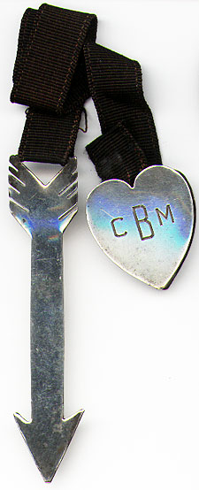 This bookmark was made in the US by an unknown manufacturer. It is marked Sterling and has a number AT180112. It is an arrow and a heart with a ribbon in between, where the heart is a clip that attaches to the binding and the arrow marks the page. The date is 1930 - 1950.