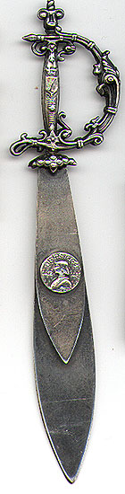 This bookmark was made in France between 1900 - 1910. It is a replica of Joan of Arc's sword with a very ornate handle and a round medalion on the smaller blade (magnified above). The medalion is a bust of Joan of Arc, the dates 1412 and 1431 and the word "Jenarre". The bookmark is silver plate over brass.