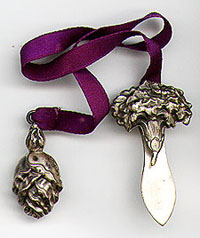 This bookmark was made in the US by Unger Bros. It is a two piece bookmark with a flower bud on one side and a blossomed flower at the other side of a purple silk ribbon. The full flower side clips over the binding of a book. It is marked with the manufacturers mark on each piece. The date is 1900 - 1910.
