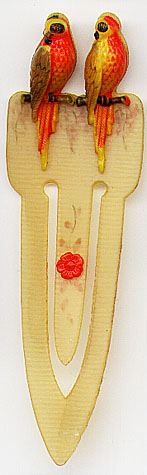  This bookmark was made in the US between 1930 and 1940. It is a celluloid piece with two parrots sitting on branches at the top. The center blade has a red flower in the middle.    