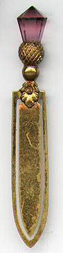  This bookmark was made in England or Scotland. It is a thistle with a purple citrine jewel on top. It is made of brass. The date is 1900 - 1910.     