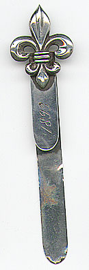 This bookmark was made in the US by Thomas F. Brogan of New York. It is marked with the makers hallmark which is a 5 pointed star and the word sterling. The top is a figural fleur de lis. The date is 1893.
