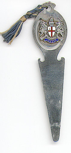 This bookmark was made in Birmingham, England in 1949. It is marked T&S and the marks for Birmingham and 1949. The top is a shield with two griffins on either end of an enamel shield with a red cross. Underneath is an enamel band with London and on top of that it says "Domine Dirige Nos." 