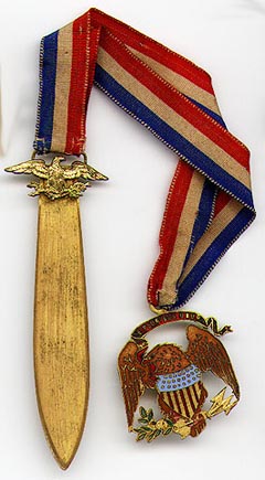 This bookmark was made in the US by an unknown manufacturer. It is marked TB on the back. It is made of bronze d'ore and enamel in two pieces separated by a red, white and blue silk ribbon. One part of the bookmark is an enameled eagle and the other side is a blade with a figural eagle on top. The date is 1920 - 1940.  