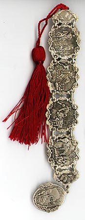 This bookmark was made in the US by an unknown manufacturer. It is a set of medallions depicting scenes from Shakespeares plays linked together with a medallion at the bottom of the head of Shakespeare himself. The other end has a large red tassel. The date is 1960 - 1970. 