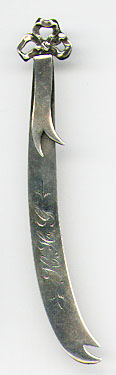 This bookmark was made in the US by Shiebler. It is marked with the manufacturers hallmark and the number 4365. It is in the shape of a ribbon with a bow at the top. The date is 1890 - 1900. 