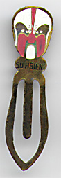 This bookmark was made in China. It is made of tin and enamel paint and has a white and pink Chinese mask on top. Underneath the mask is written "Su Hsien". The date is 1970 - 1980.  