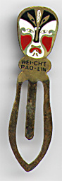 This bookmark was made in China. It is made of tin and enamel paint and has a white blue and red Chinese mask on top. Underneath the mask is written "Wei-Ch'e Pao-Lin". The date is 1970 - 1980.  