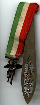 This bookmark was made in Italy. It is unmarked and is made of an unknown metal, possibly brass. It is a two piece bookmark separated by a green, white and red ribbon, the colors of the flag of Italy. One side is a pierced blade and the othe is a figural angel. The date is 1900 - 1910.  