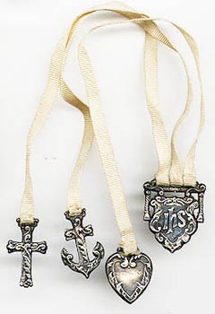 This bookmark was made in the US by an unknown manufacturer. It is marked sterling. It is a multi-page bookmark with three charms attached to ribbons. The charms are a cross, an anchor and a heart representing faith, hope and charity. The top is a piece of silver with the letters "i h s". This bookmark was sold in the 1901 Daniel Low & Co. Silver Catalog. The date is 1900 - 1910.  