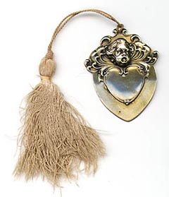 This bookmark was made in the US by Gorham. It is marked with the Gorham hallmarks and B1573M and the date mark for 1898. It is a heart shaped bookmark with a cherub on top finished in a gold wash. The original tassel is attached on top.