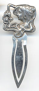  This bookmark was made in the US by Unger Bros. It is marked with the makers hallmark on the back. It is in the shape of a a woman head with long flowing hair looking at an iris flower caught in her hair. This bookmark can be found in the 1904 Unger Bros. catalog.  