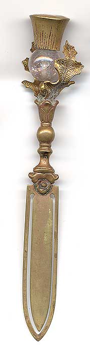  This bookmark was made in England or Scotland by an unknown manufacturer. It is brass with a rose quartz marble crystal surrounded by thistle leaves and a thistle on top. The date is 1890 - 1910.   