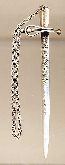  This bookmark was made in the Birmingham, England by Mitchell Brothers. It has two pieces, one a clip that attaches to the back binding and the other slips between the pages and is held in place by a vertical bar at the top. It is connected by a silver link chain. The date is 1907. 
