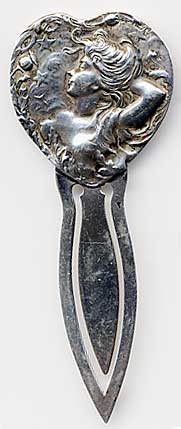 This bookmark is made in the US by Unger Bros. It is marked with the makers hallmark of an intertwined U and B. The top is a heart with an art nouveau woman whose hand is behind her head looking at the stars. The date is 1900 - 1910.  