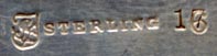 This bookmark was manufactured in the US by Towle Silversmiths. It is marked with the familiar hallmark of the T enclosing a lion along with Sterling and the number 6. On top of the 6 is stamped the number 17. This is a very interesting piece because the front is a very detailed relief of a rose and the back has a scored picture of a woman with a feather hat. The date is 1890 - 1920.