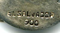 This bookmark was made in El Salvador. It is marked 900 and El Salvador. It is in the shape of a coffee leaf with a coffee bean and another leaf on top.