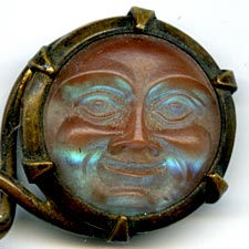 This bookmark was made in Europe, possibly France. The top is a medallion made of saphiret glass in the shape of a moon face caricature. It is a brass bookmark with a dorè finish. The date is 1870 - 1900. 