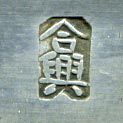 This bookmark was made in China. It is hallmarked with a Chinese symbol. The top has blue enamel with green and red flowers surrounding a brownish stone. The blade has inscribed enameled flowers.