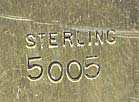 This bookmark was made in the US by an unknown manufacturer. It is marked sterling 5005 on the back. This is a two-toned silver bookmark where the top blade is a figural man in the moon in white silver and the bottom blade is finished in a gold wash in the shape of a spade. The top has a fleur-de-lis. The date is 1892.   