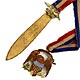 This bookmark was made in the US by an unknown manufacturer. It is marked TB on the back. It is made of bronze d'ore and enamel in two pieces separated by a red, white and blue silk ribbon. One part of the bookmark is an enameled eagle and the other side is a blade with a figural eagle on top. The date is 1920 - 1940.  