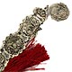 This bookmark was made in the US by an unknown manufacturer. It is a set of medallions depicting scenes from Shakespeares plays linked together with a medallion at the bottom of the head of Shakespeare himself. The other end has a large red tassel. The date is 1960 - 1970. 